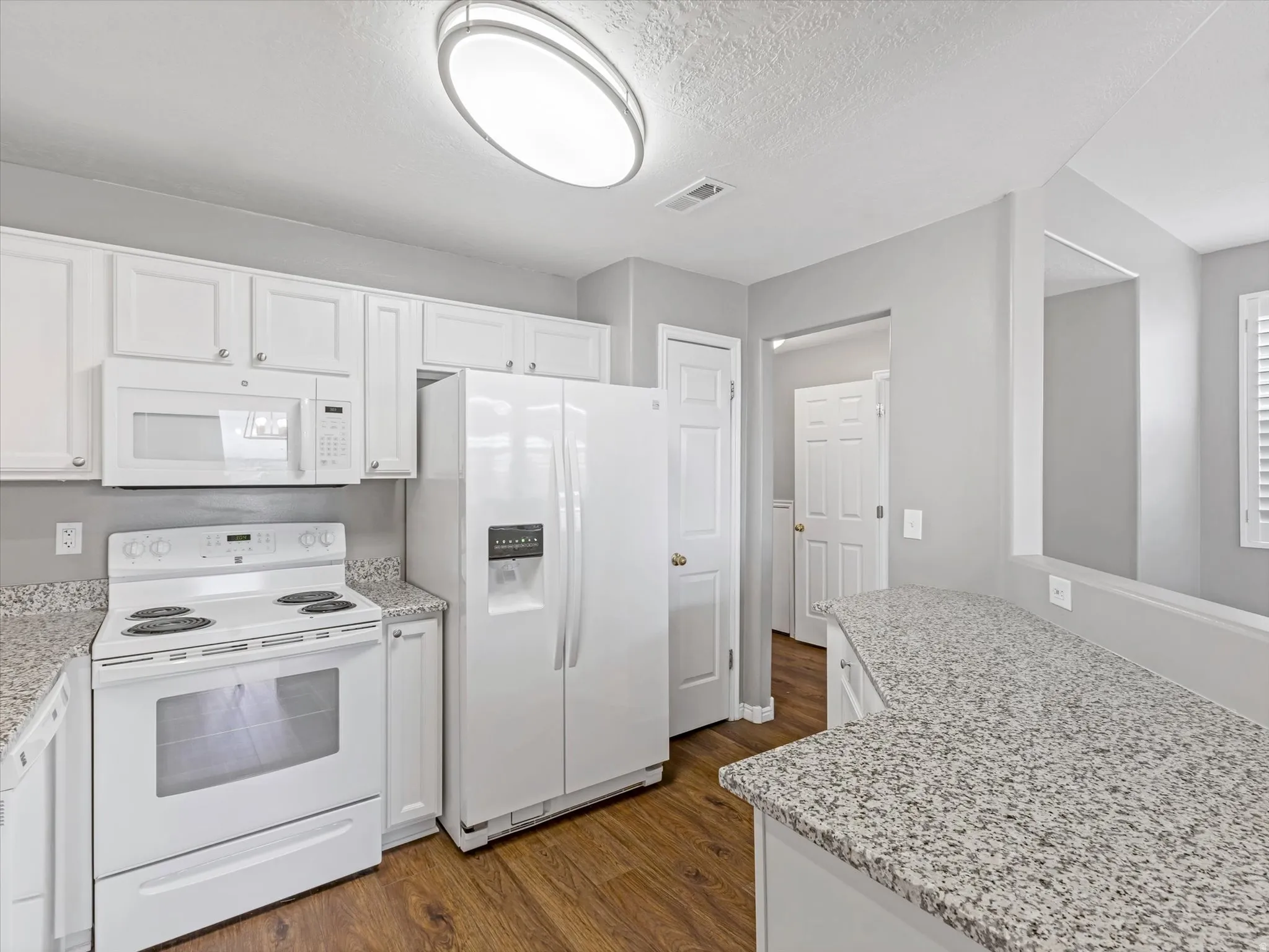 Contemporary kitchen with white cabinetry and appliances, granite-style countertops, wood-finish flooring, and recessed lighting