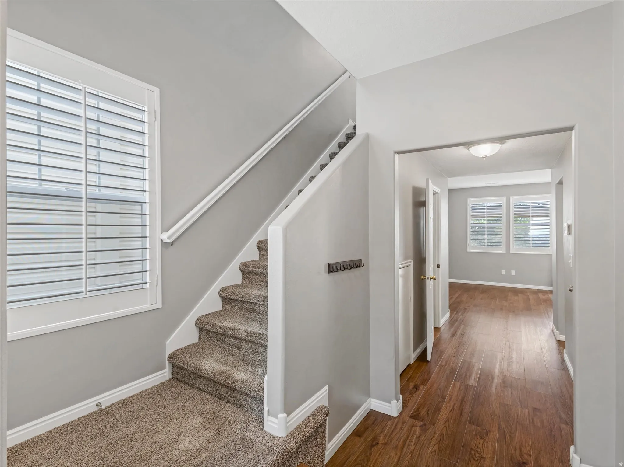 Staircase with plush carpeting and white railing, featuring a large window with plantation shutters