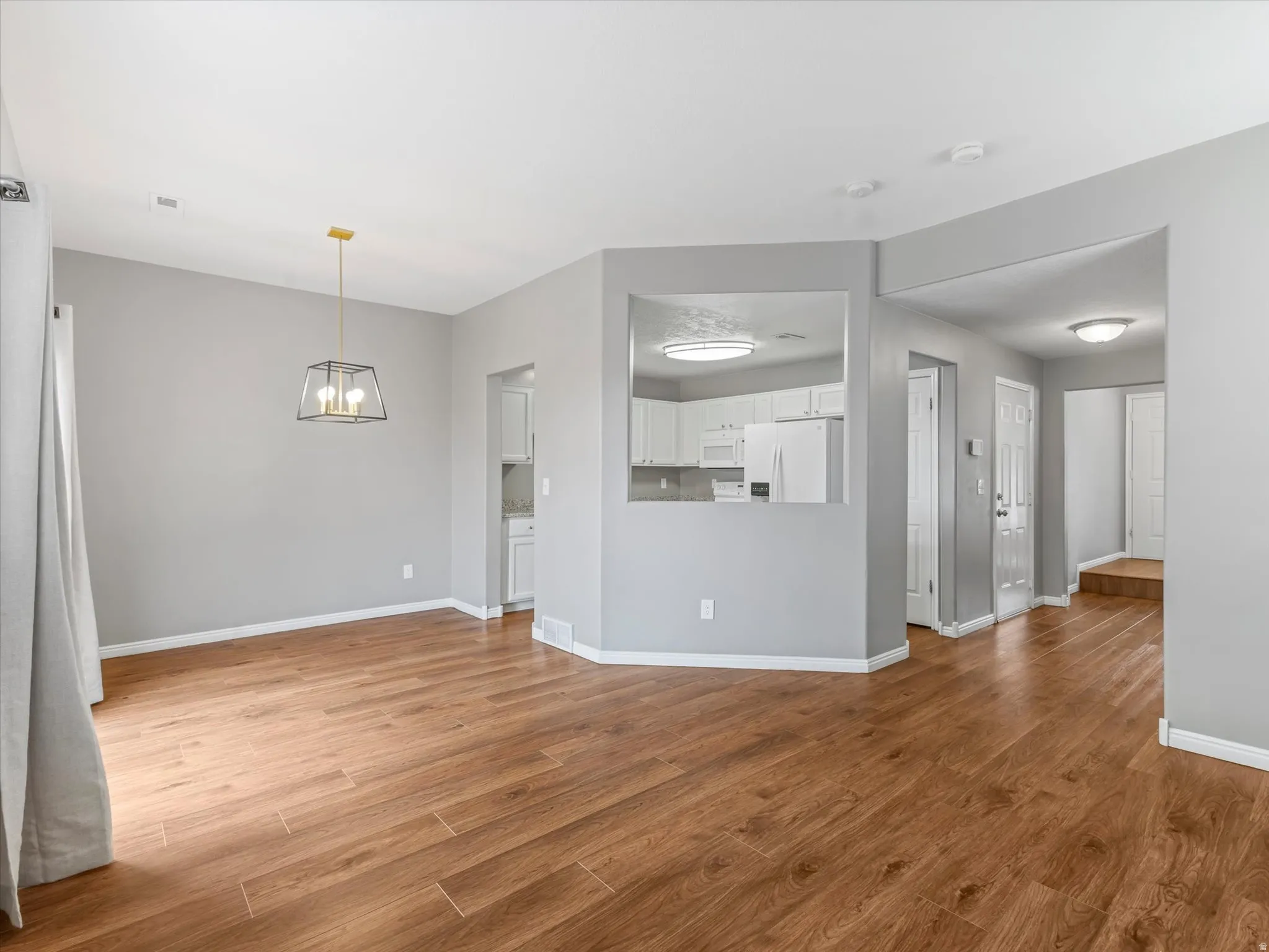 Open-concept living area featuring wood-finish flooring, a modern chandelier with a gold-tone accent, and light gray wall paint