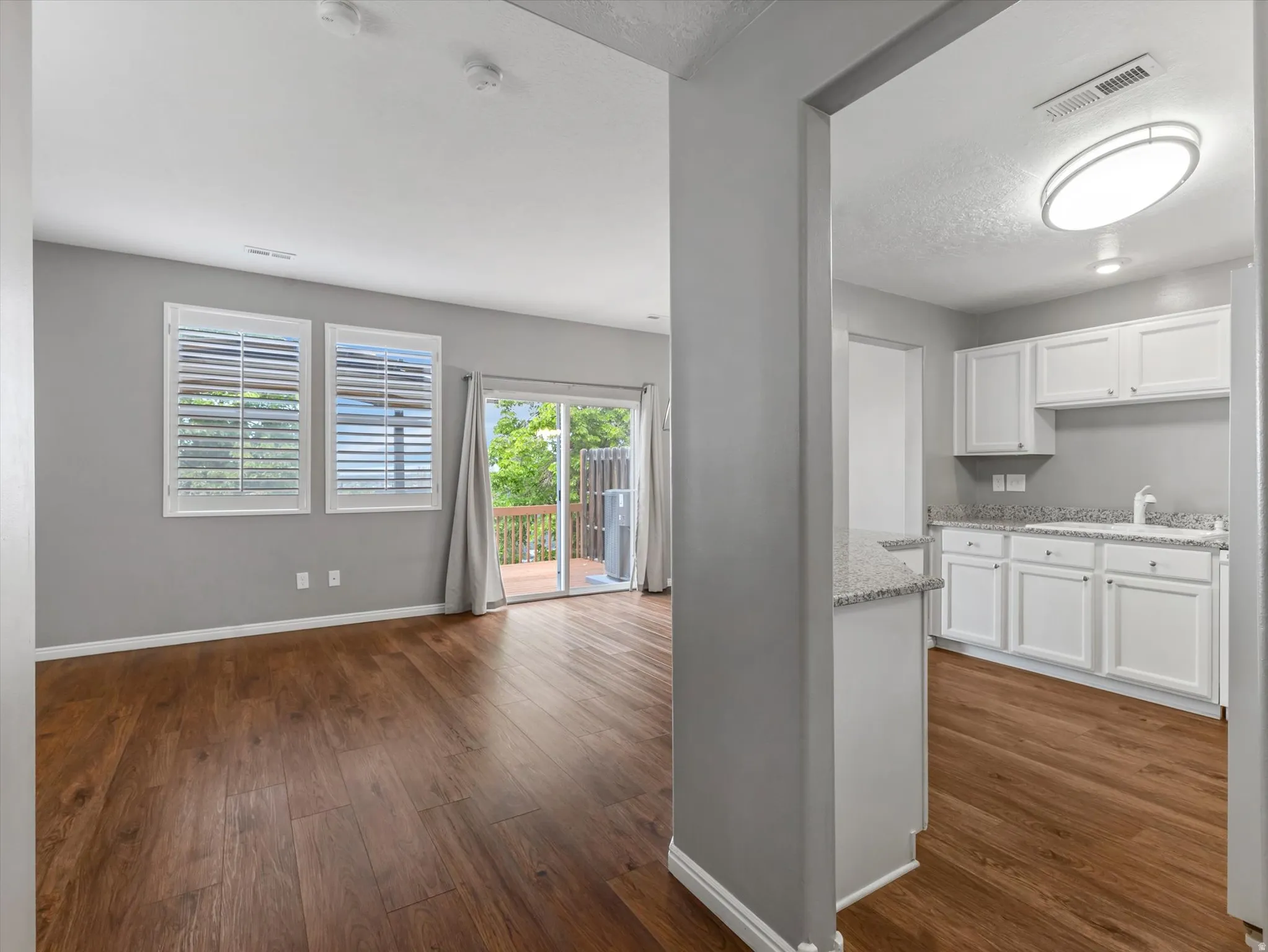 Open concept living area with wood-finish flooring, plantation shutters, and sliding glass door access to an exterior deck