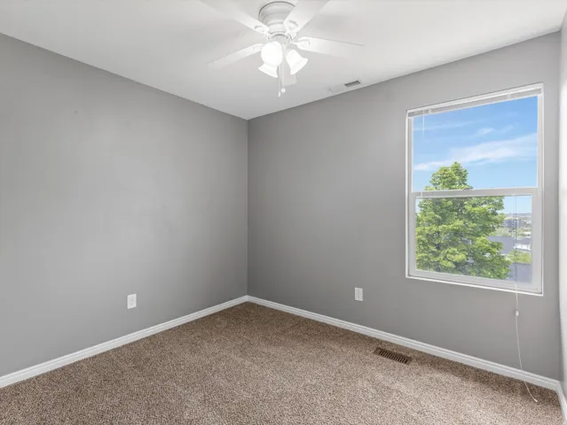 Carpeted room featuring a white ceiling fan with integrated lighting, a single window, and light grey walls with white trim