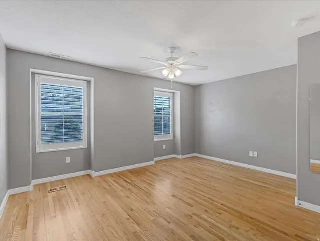 Spacious room with wood-finish flooring, two windows with white blinds, and a ceiling fan with integrated lighting
