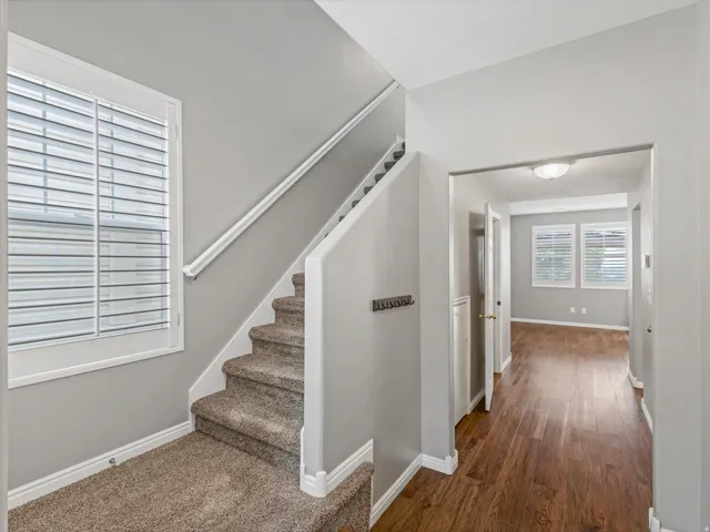 Staircase with plush carpeting and white railing, featuring a large window with plantation shutters