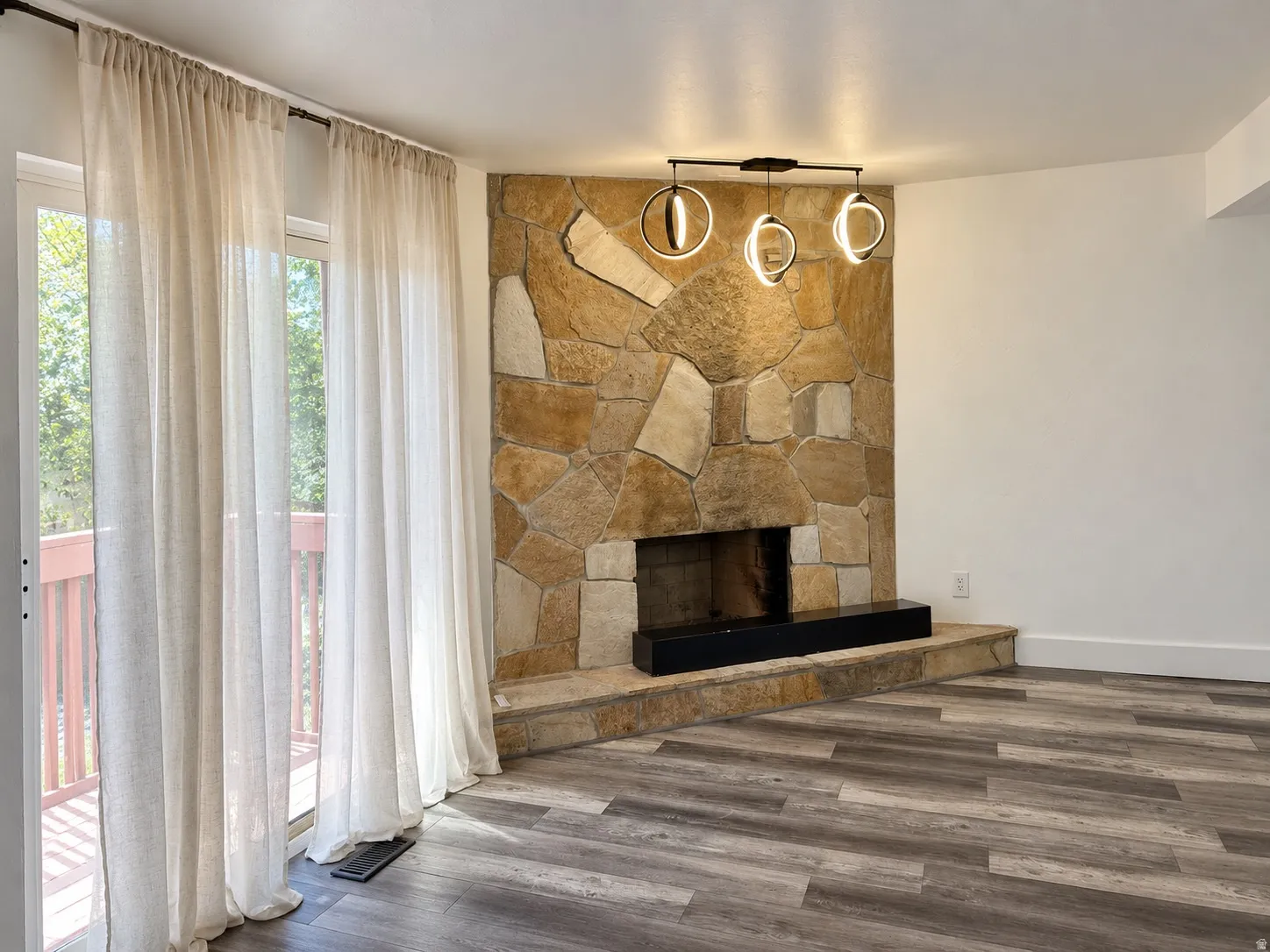 Stone-clad fireplace with hearth, modern linear chandelier, wide plank wood-finish flooring, and sliding glass door