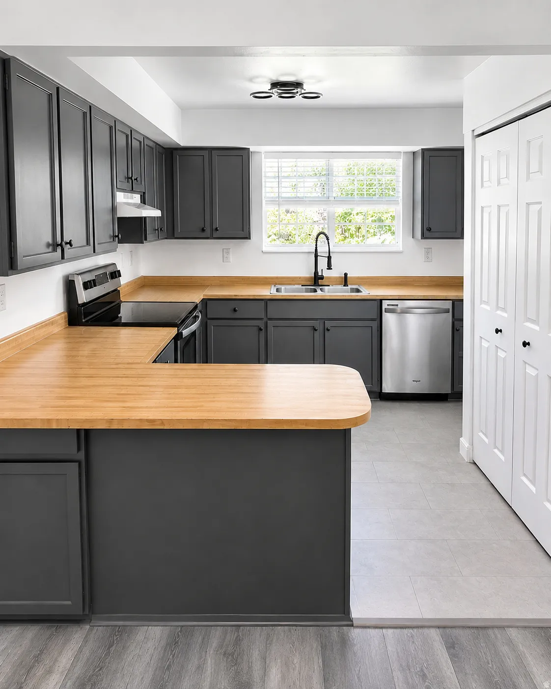 U-shaped kitchen featuring charcoal cabinetry, wood-finish countertops, stainless steel appliances, a black pull-down faucet, and a modern ceiling light fixture