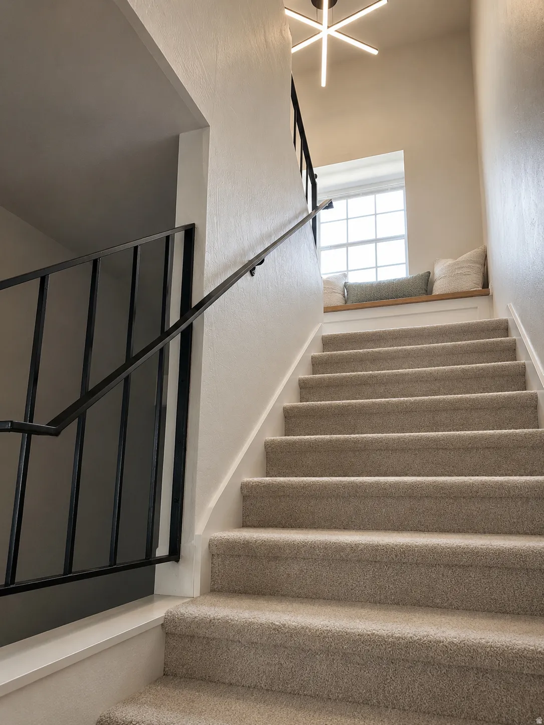 Carpeted staircase with black metal railing, window with built-in wood-finish bench, and a modern ceiling light fixture