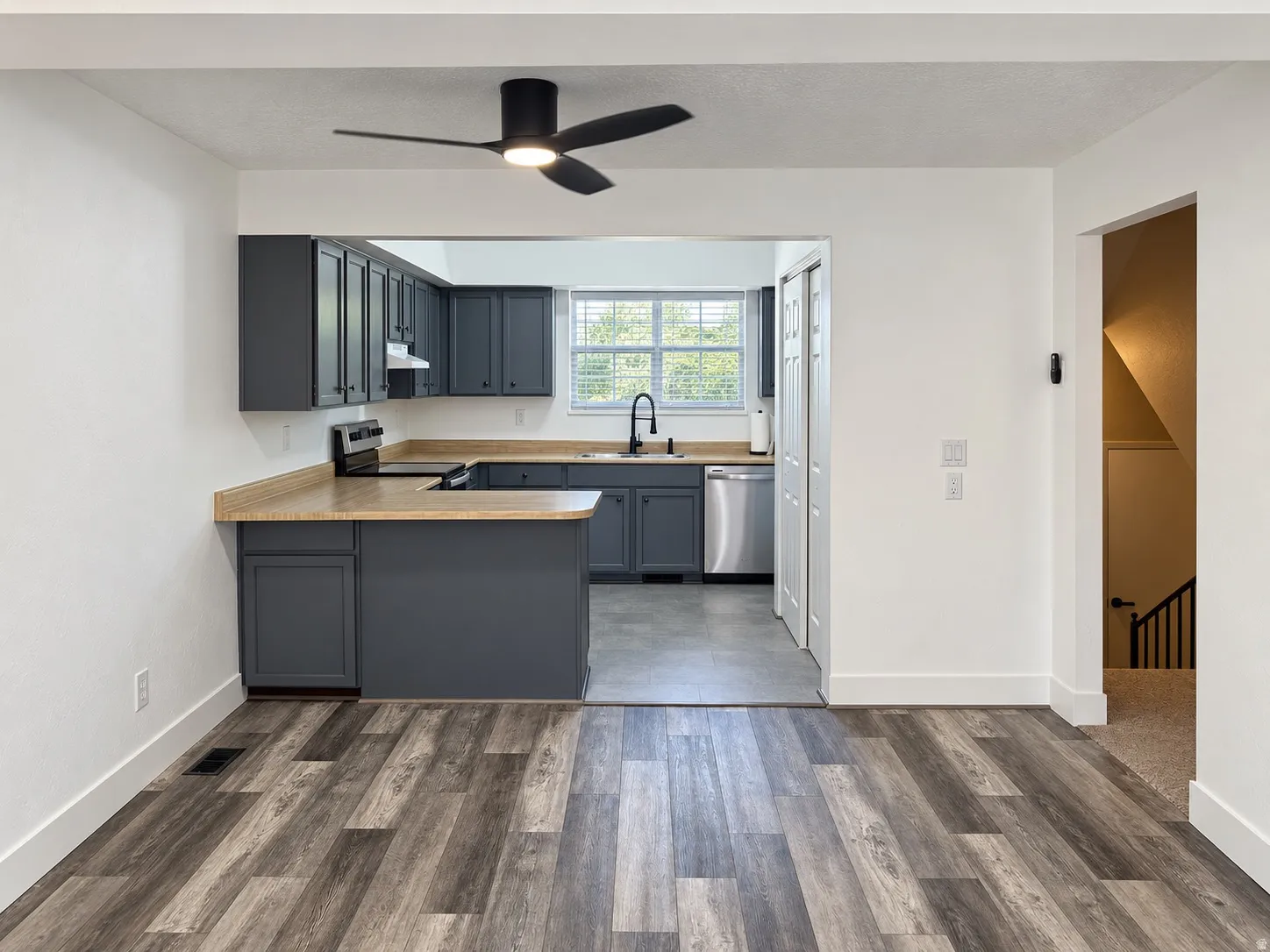 Kitchen featuring dark cabinetry, stainless steel appliances, wood-finish countertops, and a modern ceiling fan with lighting