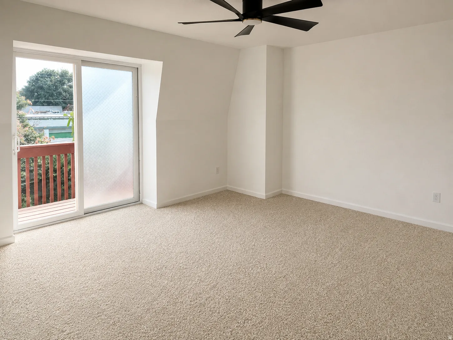Sliding glass door leading to an outdoor balcony with a wooden railing, neutral carpeting, and a ceiling fan