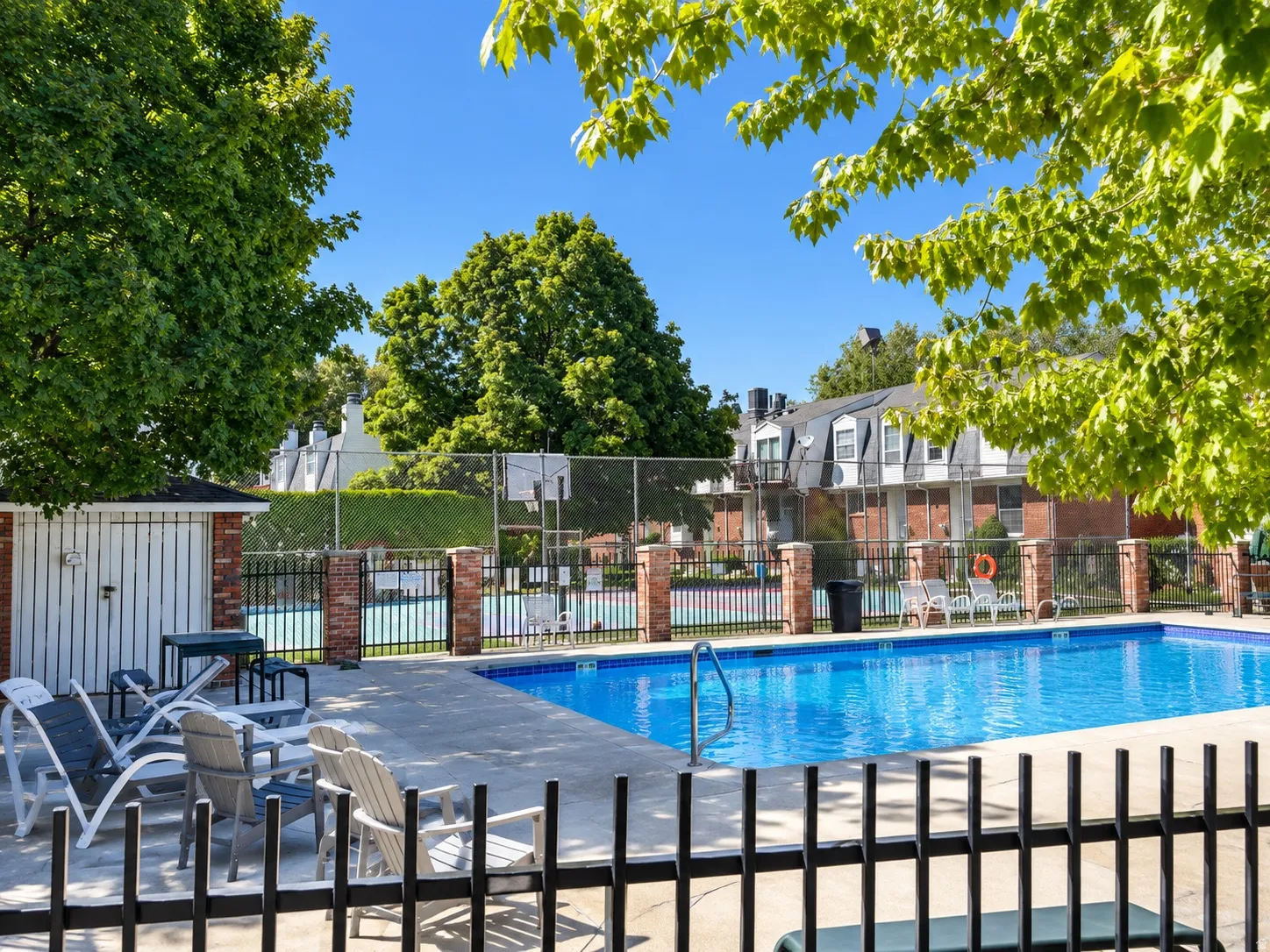Community swimming pool with concrete decking, surrounding black metal fencing, and brick pillars