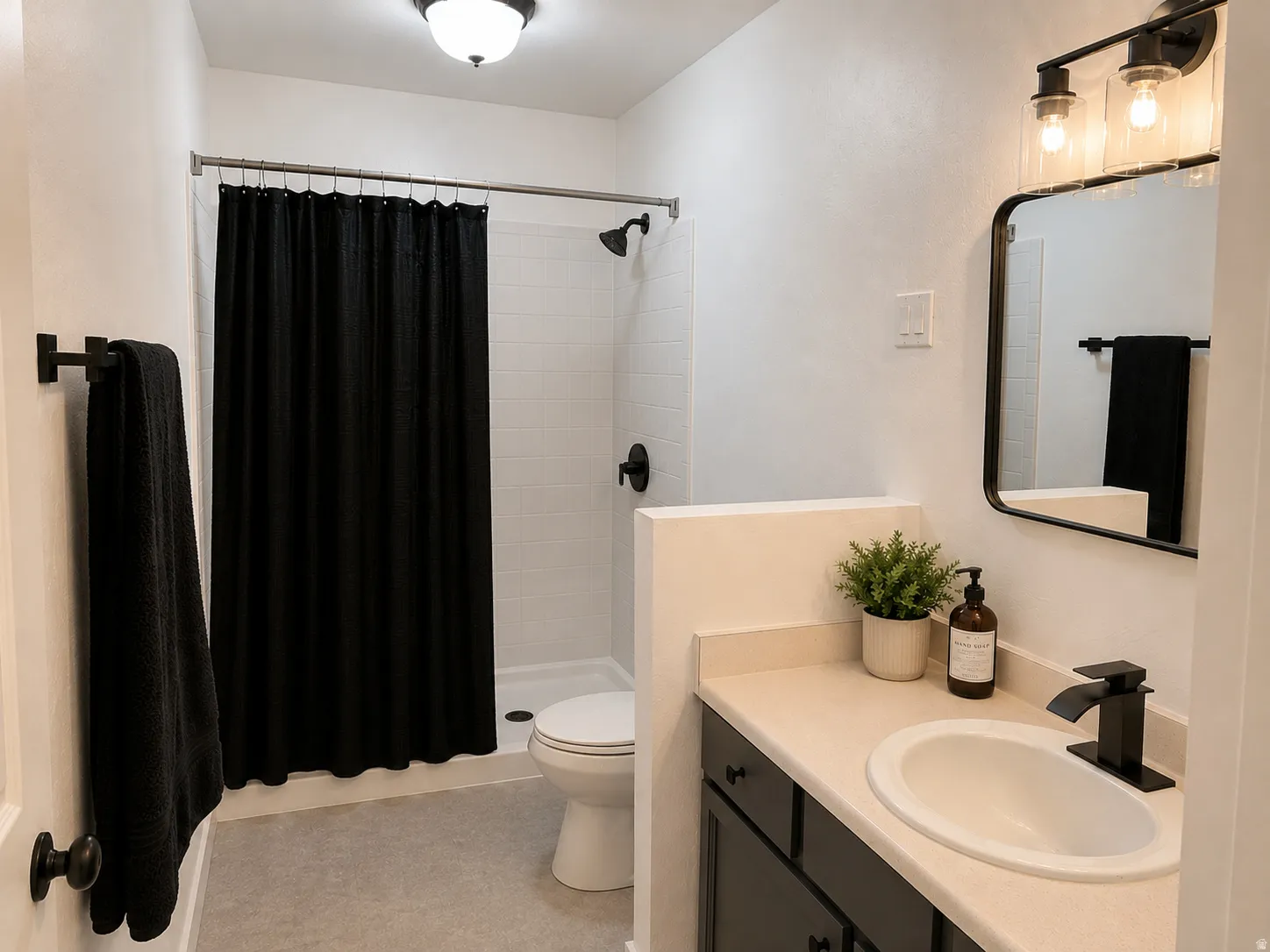 Compact bathroom featuring a shower with subway tile surround, matte black fixtures, an oval undermount sink, a light-toned countertop, and black vanity cabinetry
