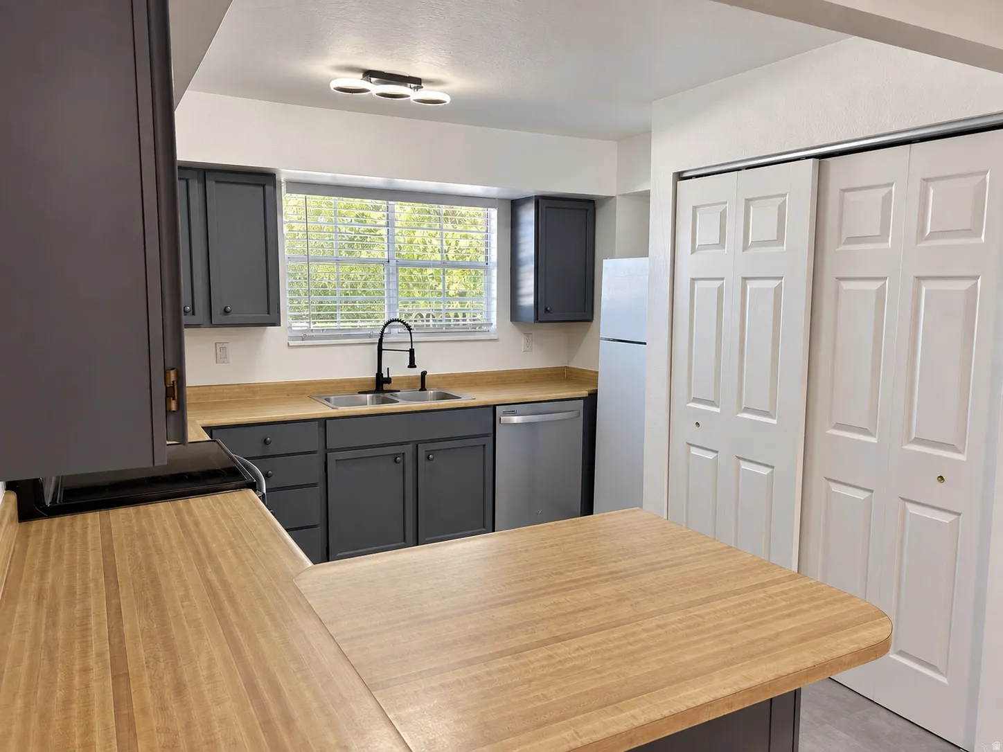 Kitchen featuring gray cabinetry, wood-finish countertops, stainless steel appliances, a double basin sink with a gooseneck faucet, and a contemporary ceiling light fixture