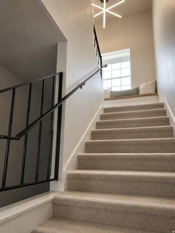 Carpeted staircase with black metal railing, window with built-in wood-finish bench, and a modern ceiling light fixture