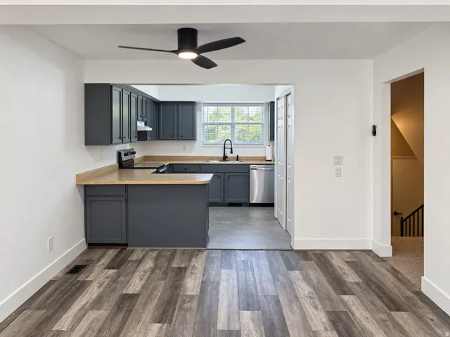 Kitchen featuring dark cabinetry, stainless steel appliances, wood-finish countertops, and a modern ceiling fan with lighting