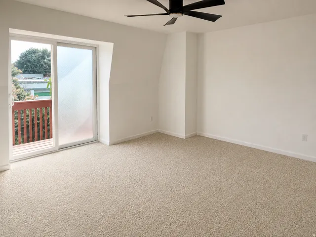 Sliding glass door leading to an outdoor balcony with a wooden railing, neutral carpeting, and a ceiling fan