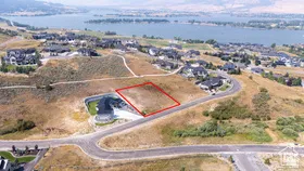 Elevated property lot outlined in red, featuring natural terrain and a backdrop of a large body of water
