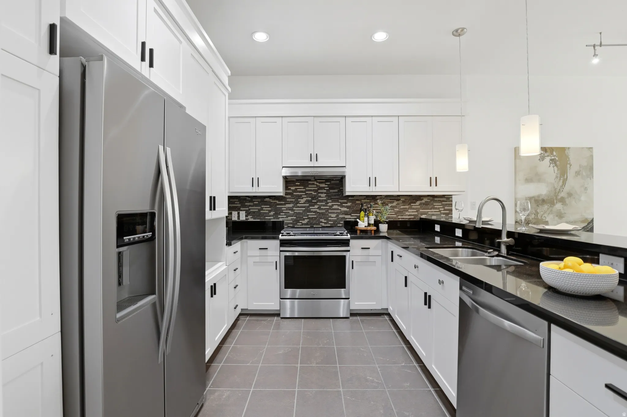 U-shaped kitchen featuring white shaker cabinetry with dark pulls, dark tile flooring, stainless steel appliances, dark countertops, and a mosaic tile backsplash