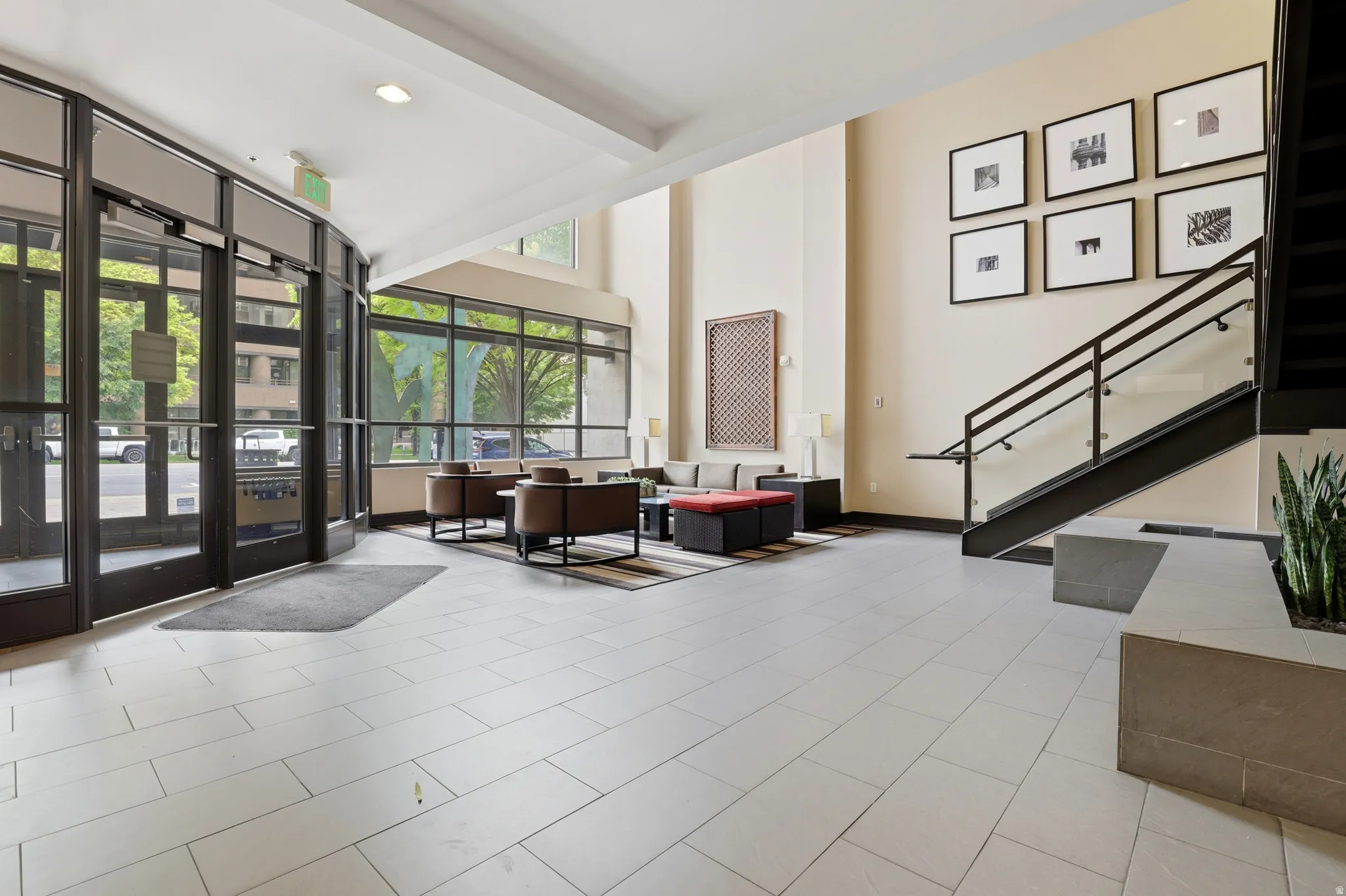 Spacious lobby featuring large format tile flooring, a contemporary staircase with glass railing, abundant natural light from extensive window walls, and high ceilings