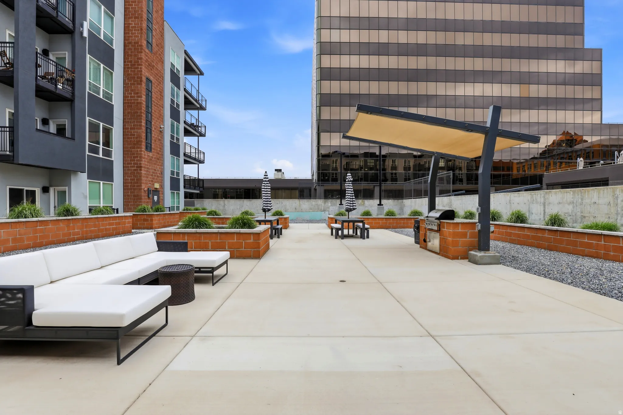 Expansive rooftop patio featuring concrete pavers, a built-in brick grilling station with a sunshade, and integrated planters with low-maintenance landscaping