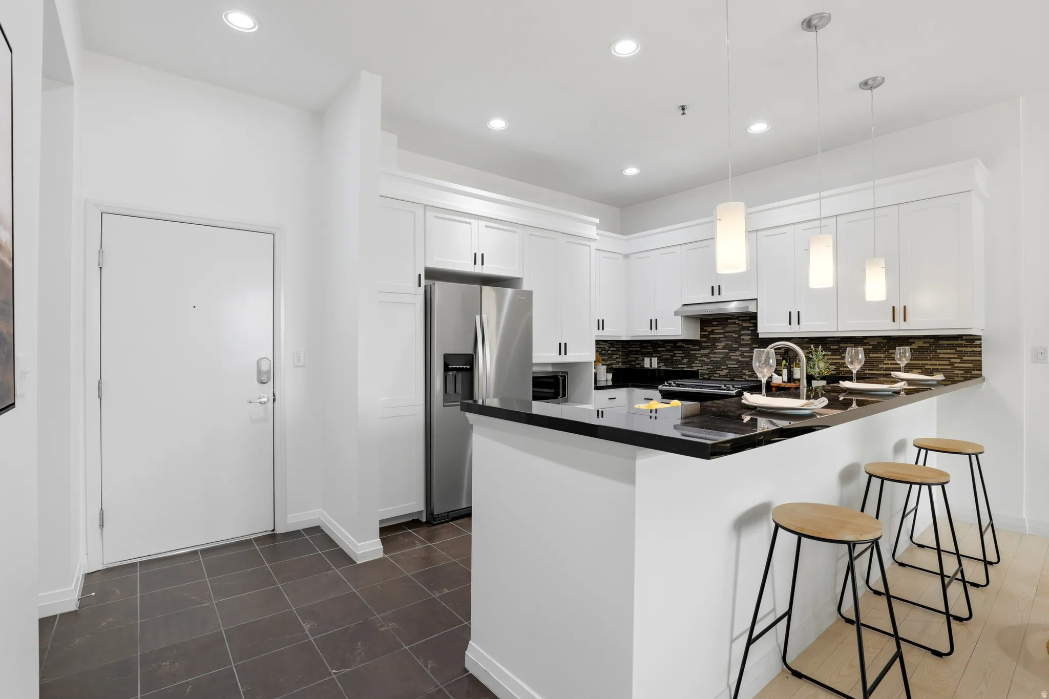 Modern kitchen featuring white shaker cabinetry, stainless steel appliances, dark countertops, and a mosaic tile backsplash