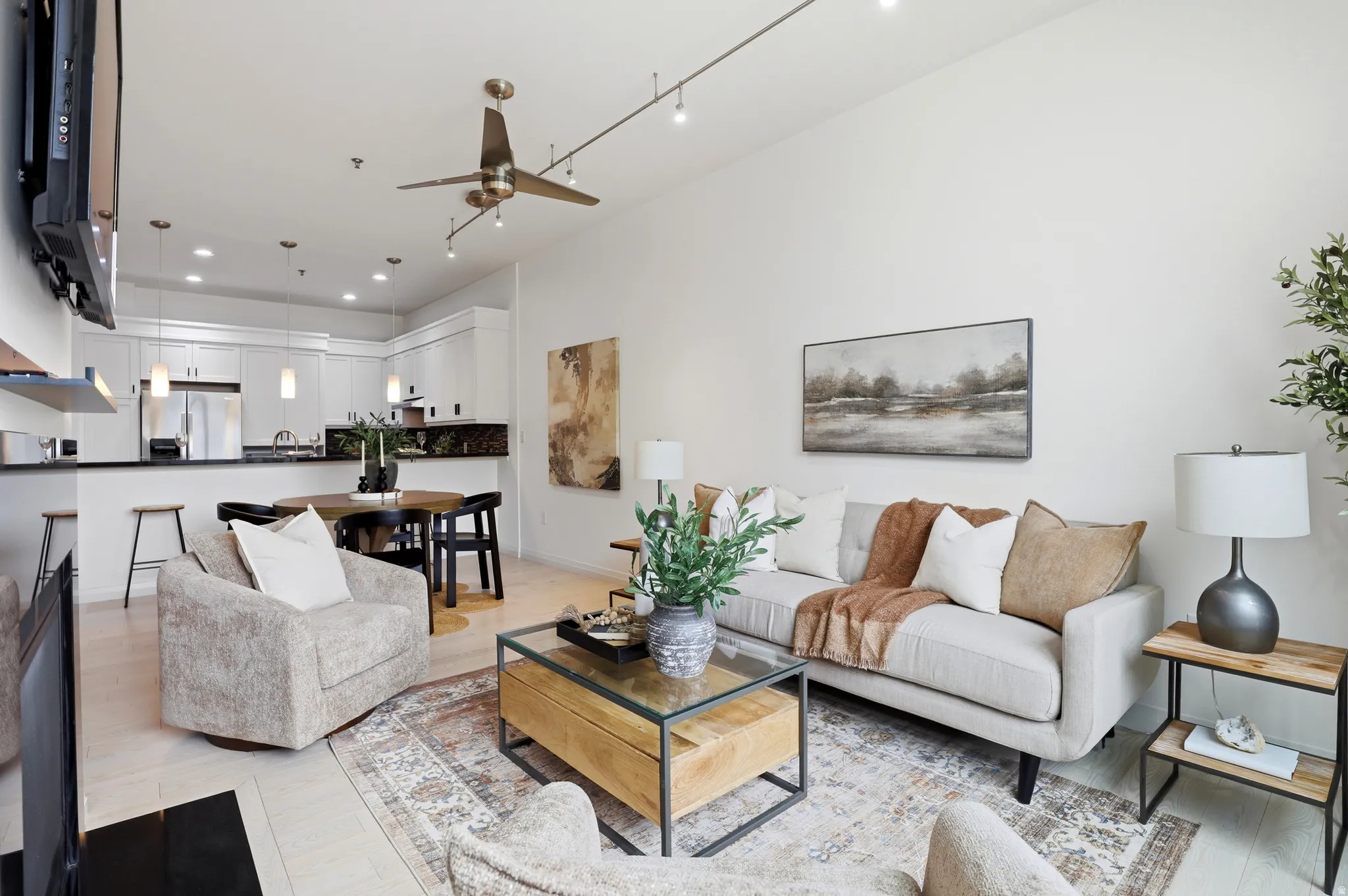 Open-concept living space featuring high ceilings, light wood-finish flooring, and a contemporary ceiling fan with track lighting