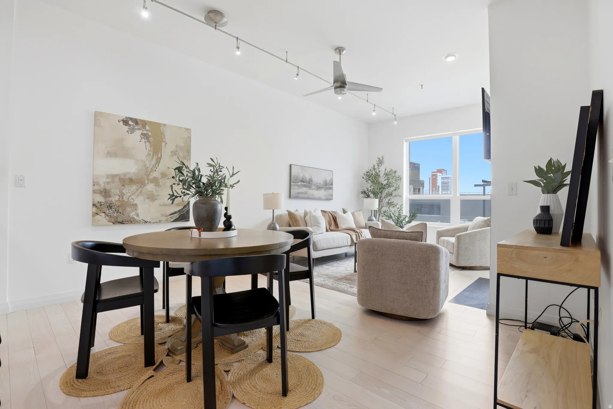 Open-concept living space with light wood-finish flooring, high ceilings, track lighting, and a contemporary ceiling fan