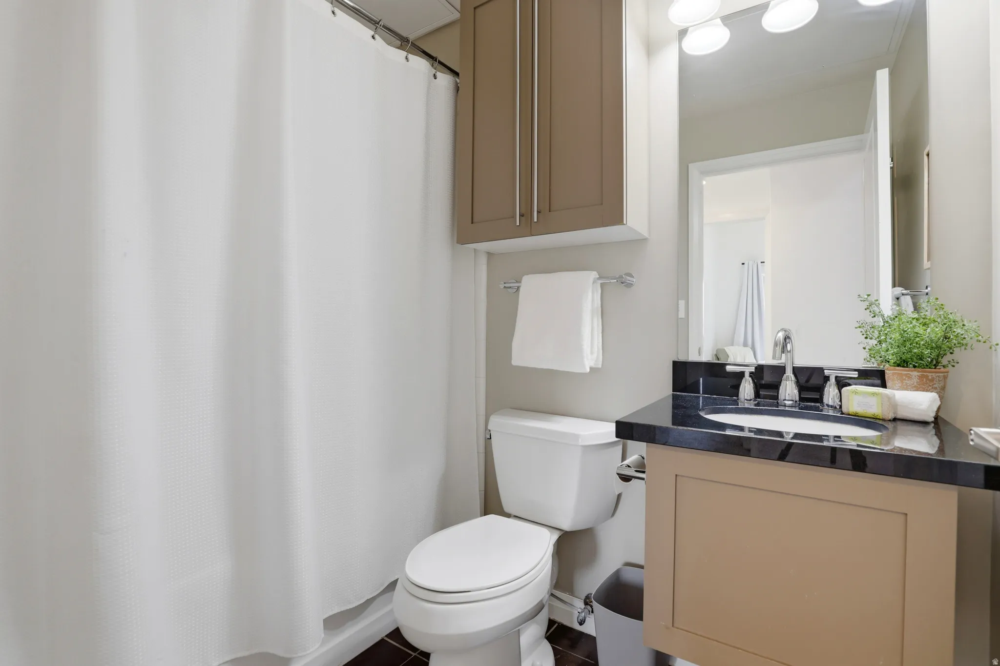 Bathroom featuring a vanity with a dark countertop and integrated sink, chrome faucet, wall-mounted mirror, and overhead lighting