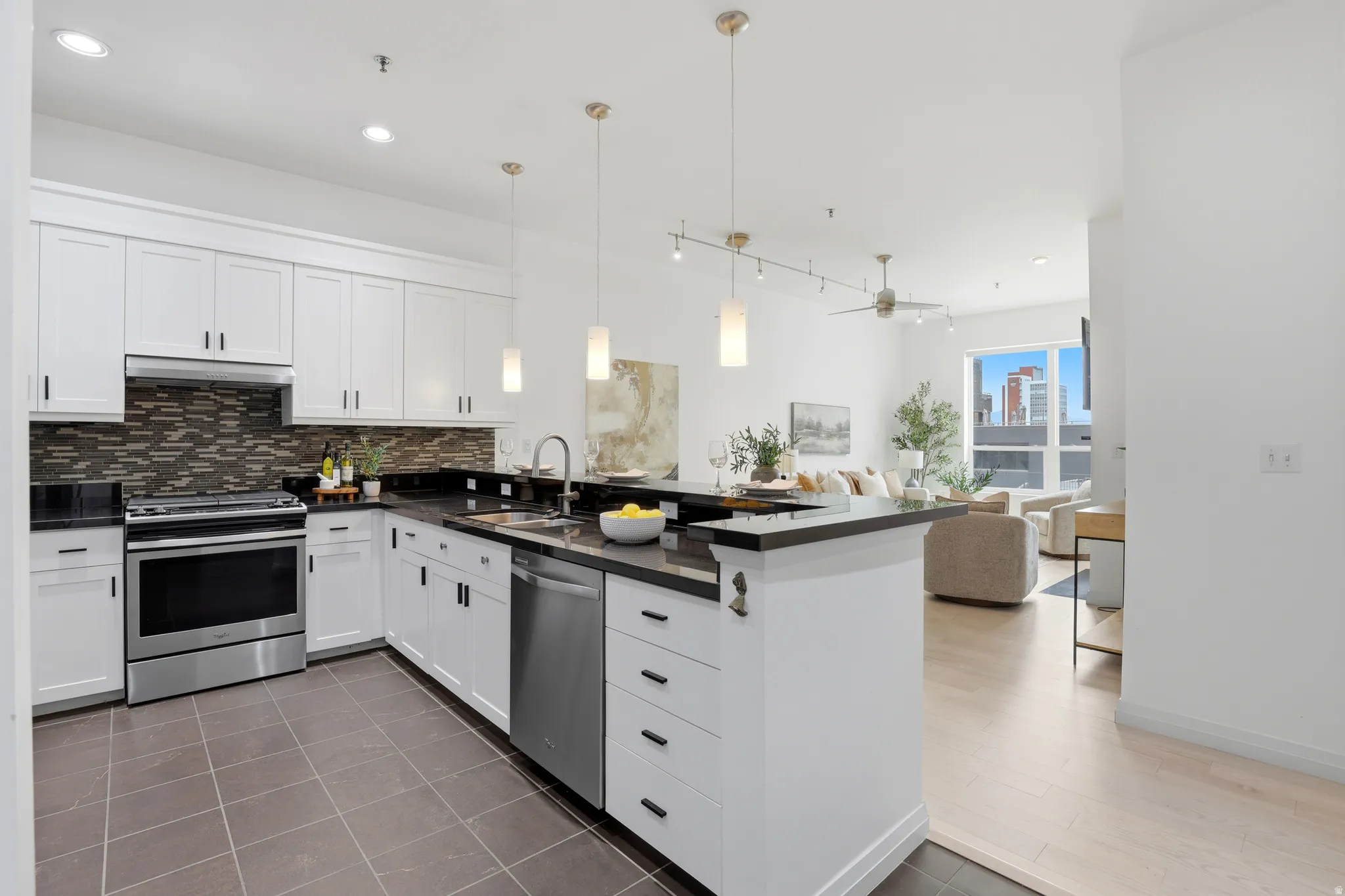 Modern kitchen featuring white cabinetry, dark countertops, tile backsplash, and stainless steel appliances, including a built-in oven range and dishwasher