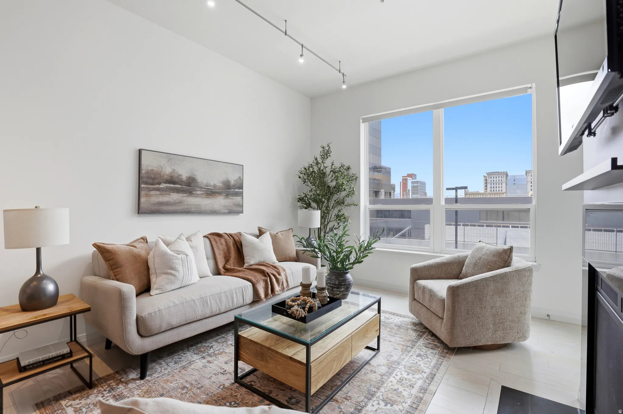 Expansive window with city buildings visible, track lighting, light-toned flooring, white walls, and a built-in fireplace feature