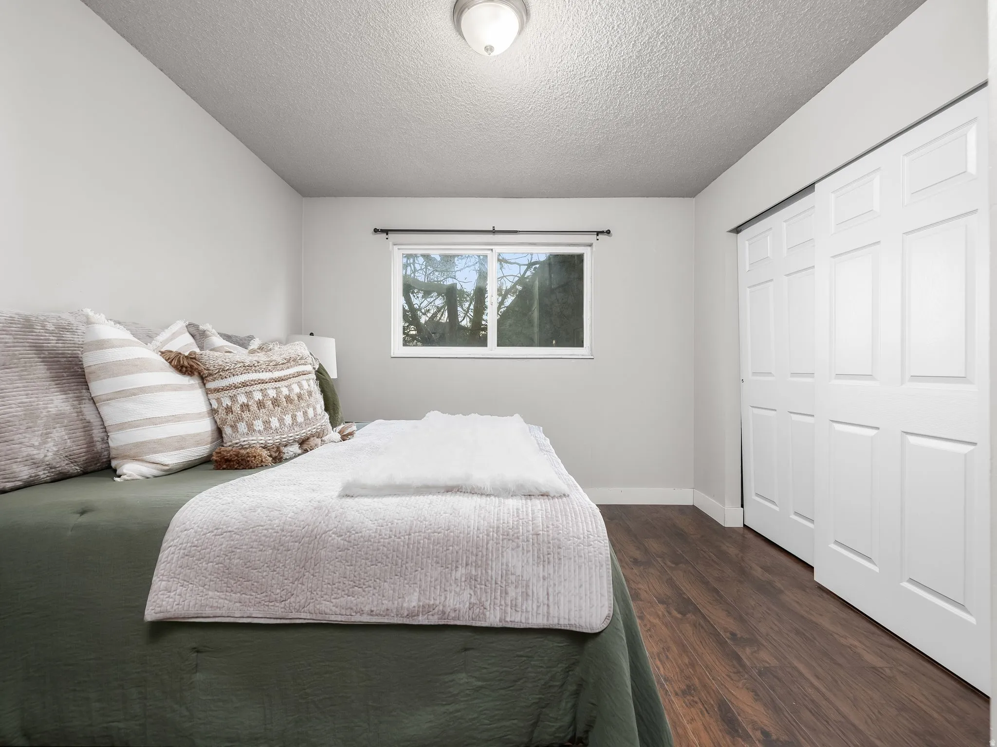 Bedroom featuring wood-finish flooring, a double-pane window, and white bi-fold closet doors