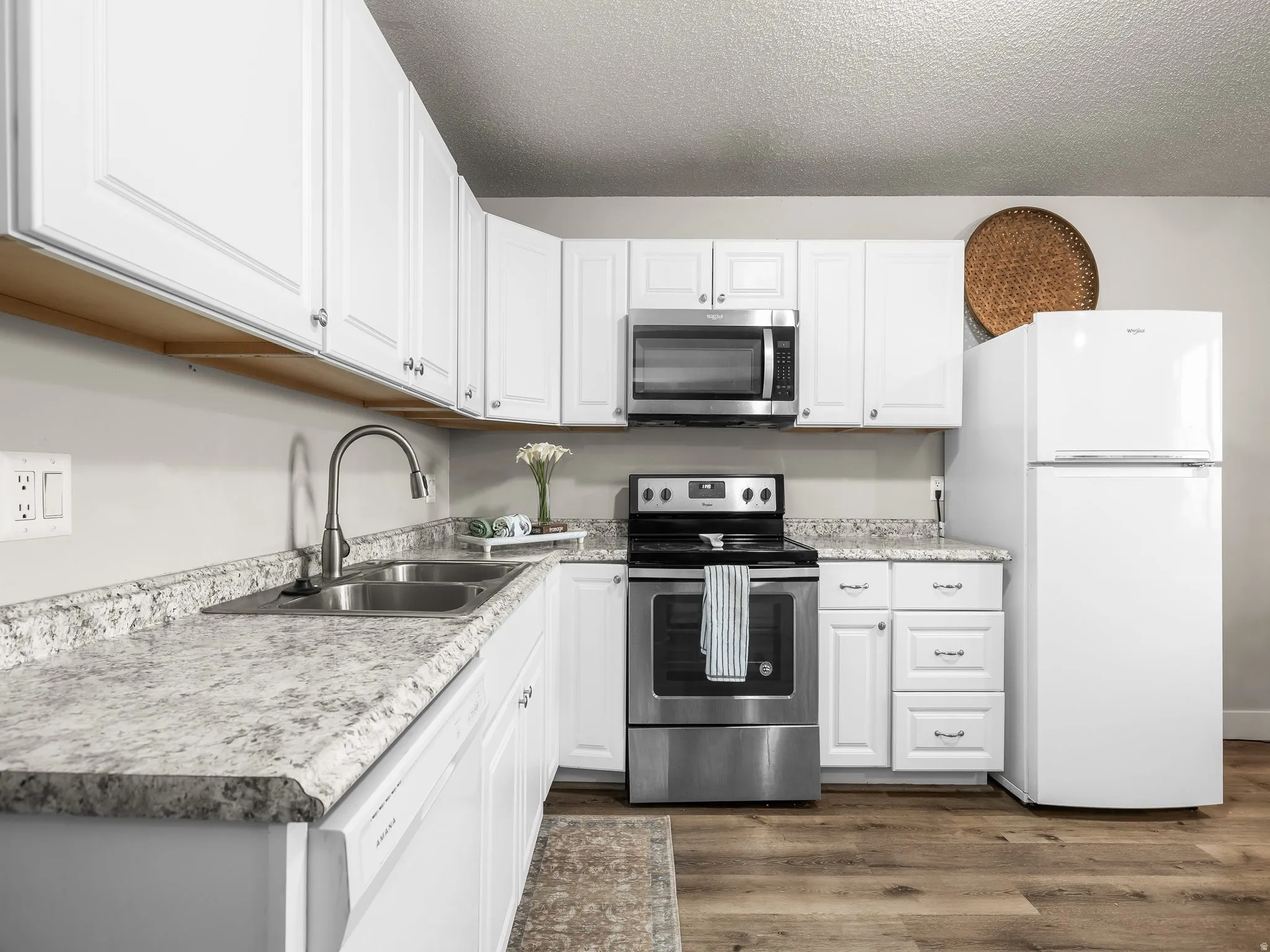 Bright kitchen featuring white cabinetry, stone-finish countertops, and wood-finish flooring