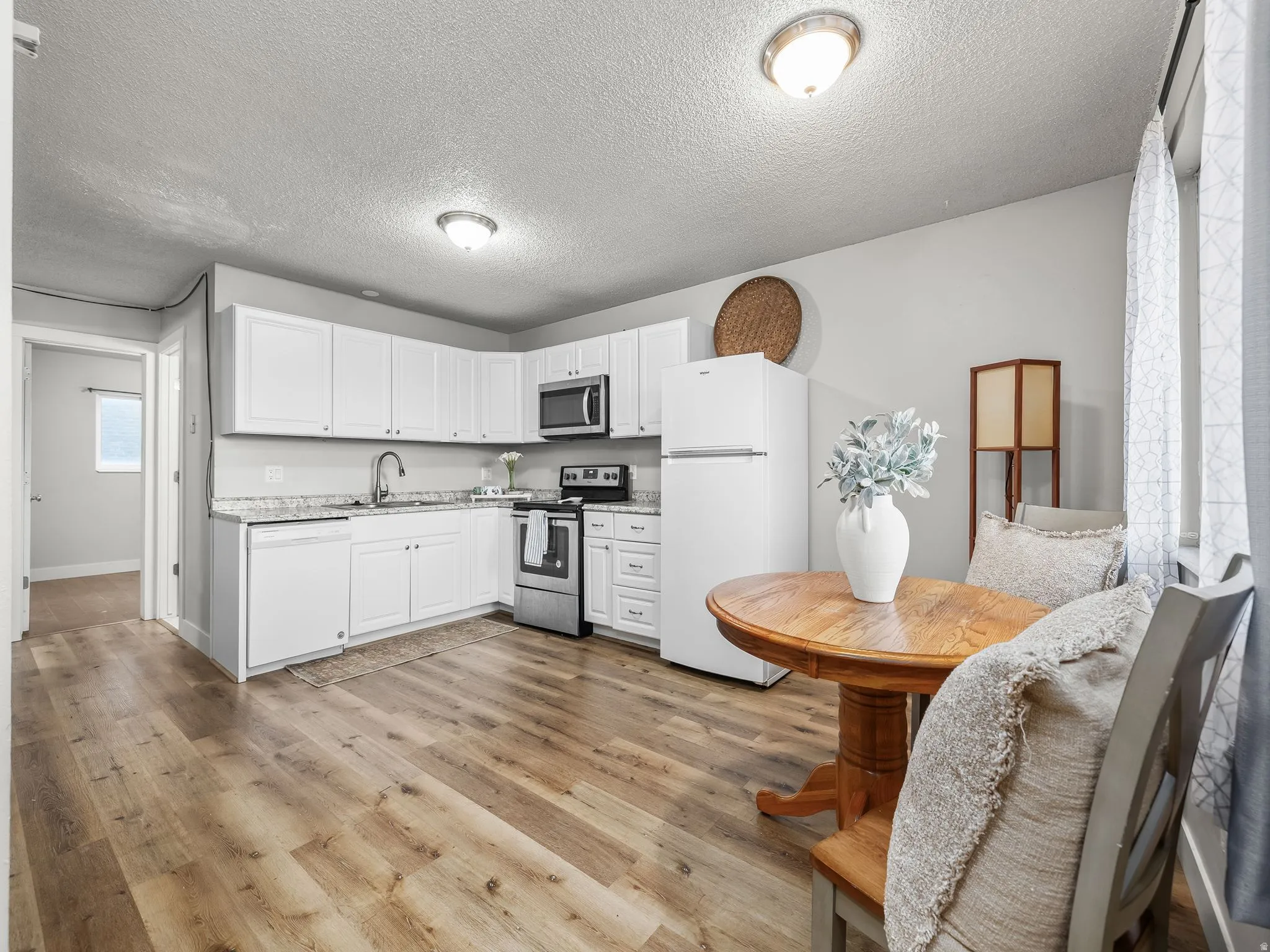 Kitchen featuring white cabinetry, light-toned wood-finish flooring, stainless steel appliances, speckled countertops, and ceiling-mounted lighting fixtures