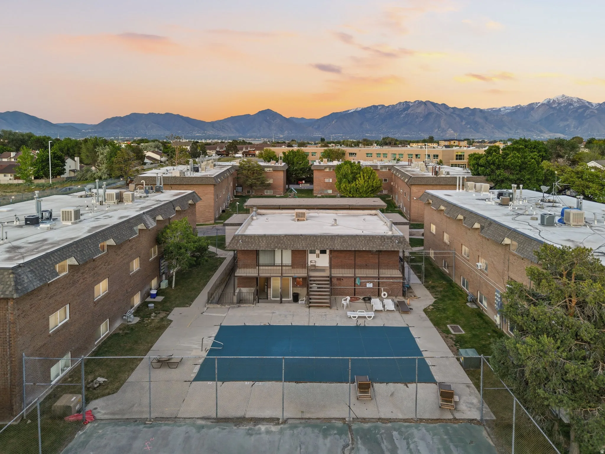 Central outdoor pool area with surrounding multi-story brick buildings, concrete patio, and fenced perimeter