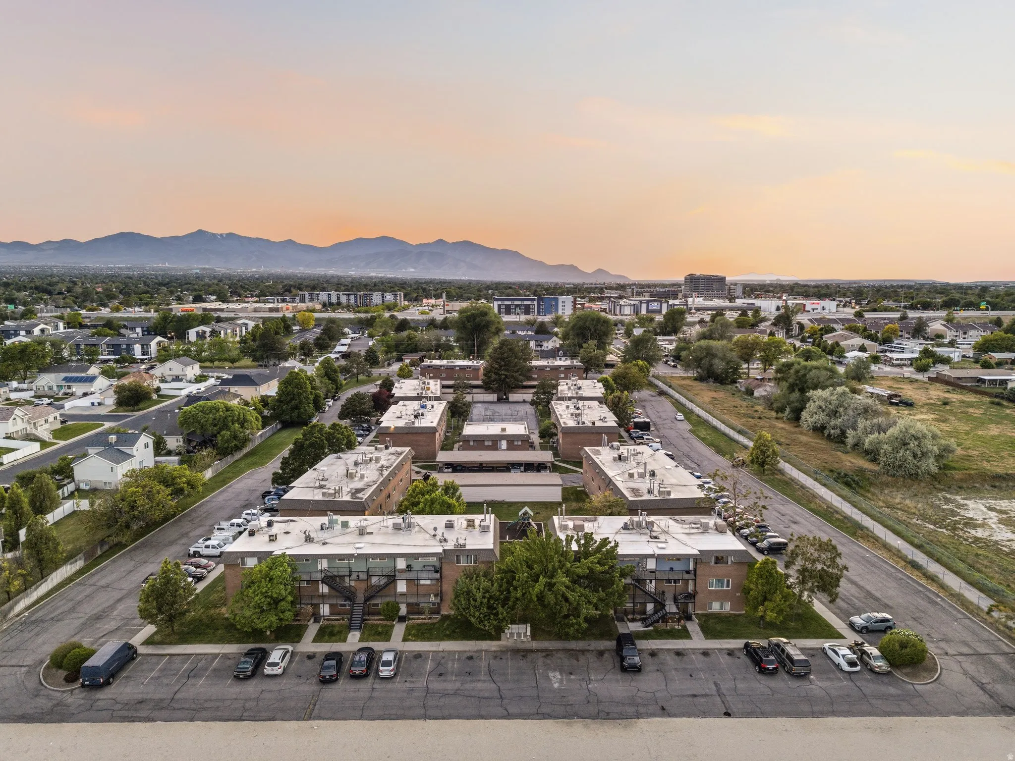 Aerial perspective of a multi-building property featuring brick and light-colored siding exteriors, extensive surface parking, and mature landscaping