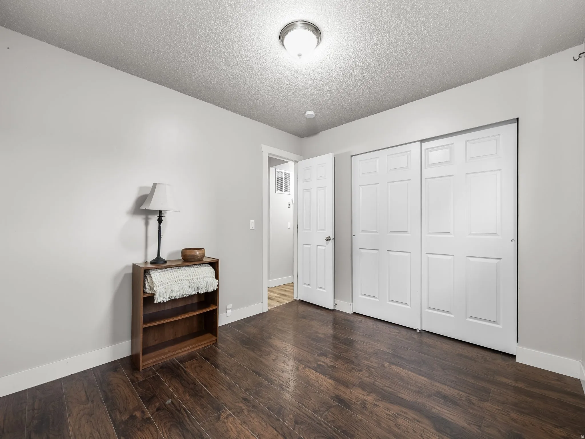 Bedroom featuring dark wood-finish flooring, light grey painted walls, white baseboards, and a white six-panel sliding closet door