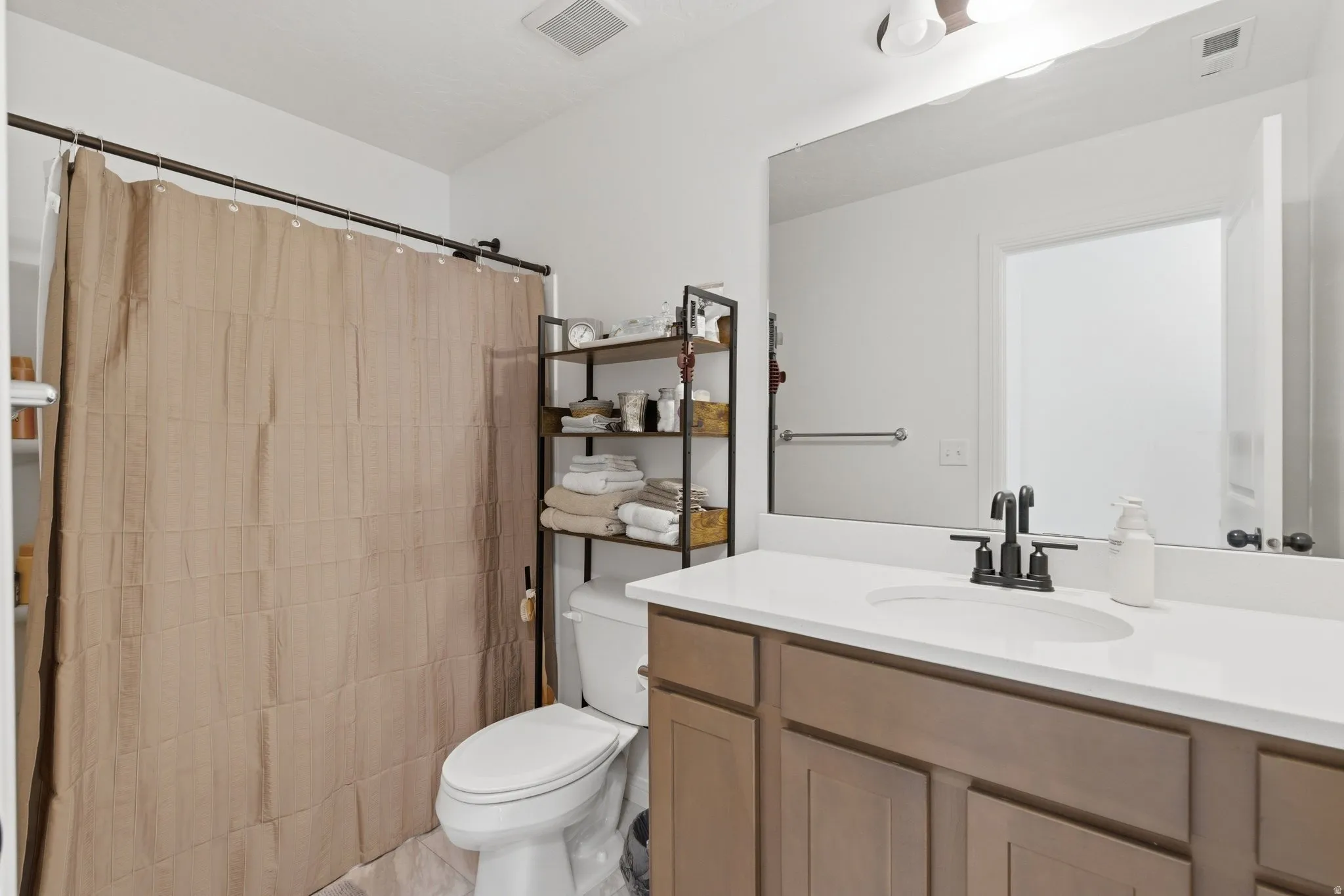 Bathroom featuring a single vanity with a white countertop and brown cabinetry, a large mirror, and a shower area with a curtain rod