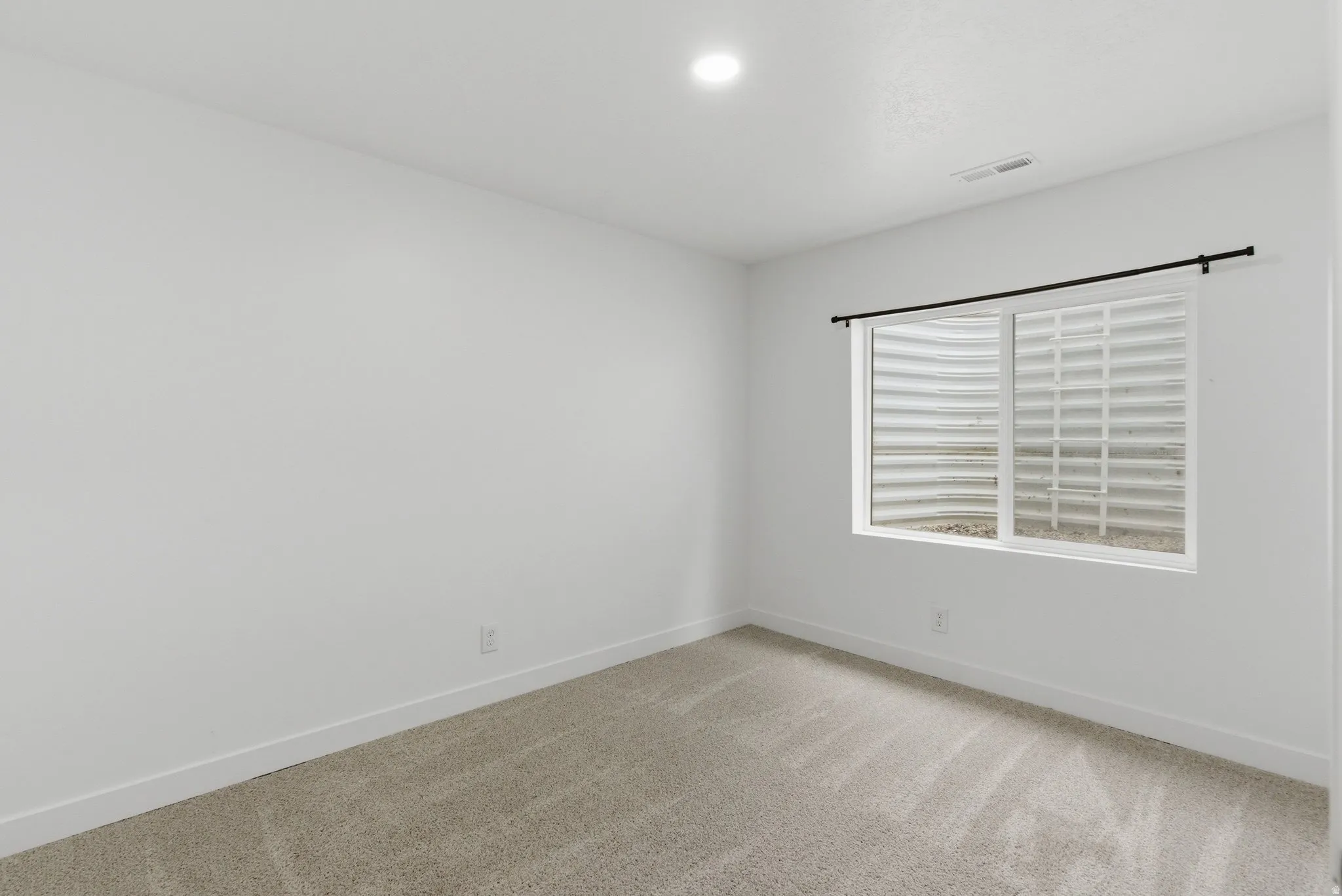 Carpeted room featuring a window with a window well, white walls, and recessed lighting