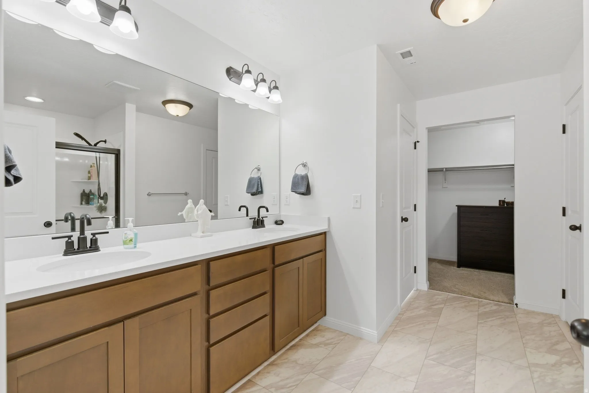 Bathroom featuring a dual vanity with white countertops and wood-finish cabinetry, illuminated by two wall-mounted light fixtures