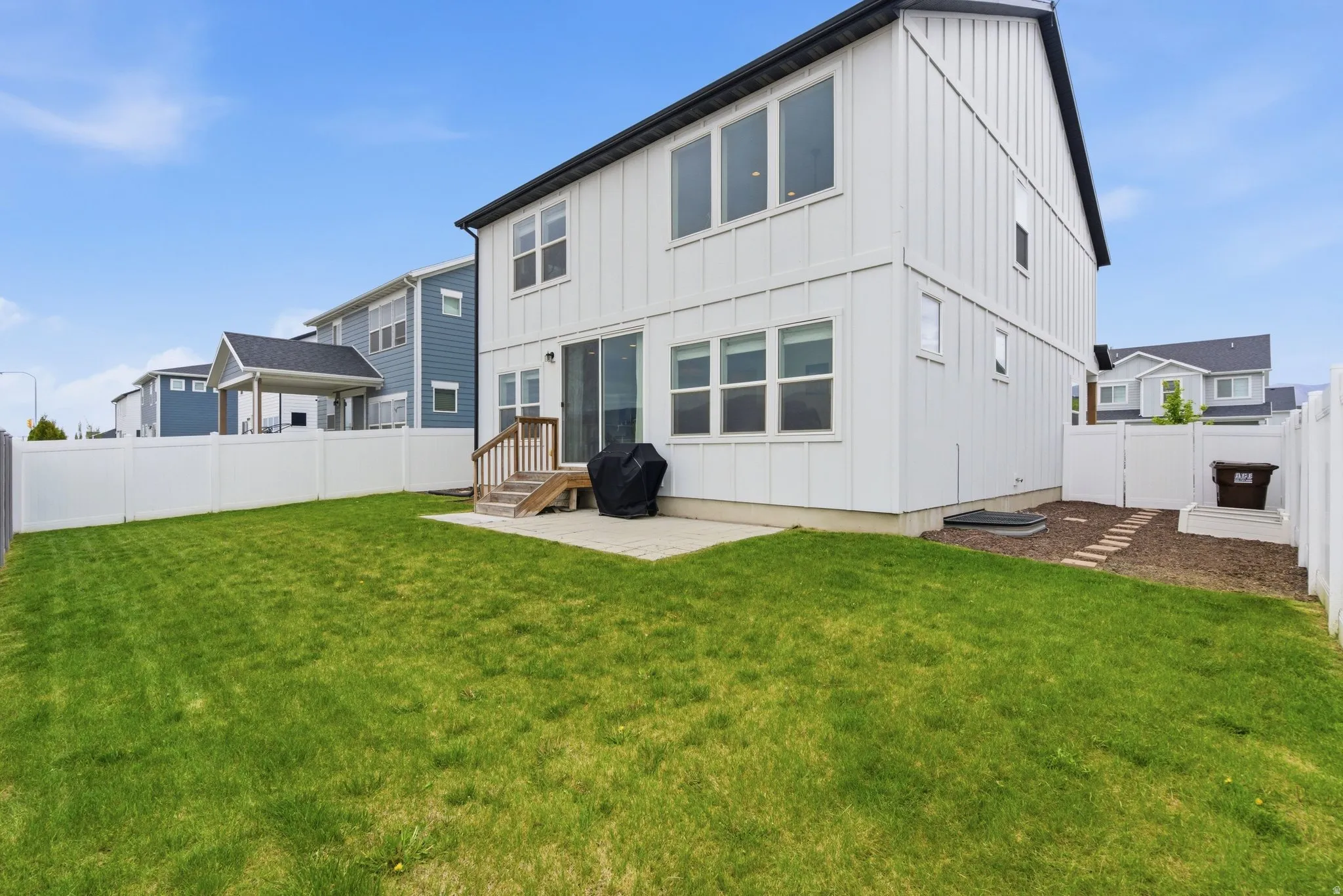 Spacious backyard featuring a large green lawn, a white privacy fence, and a concrete patio