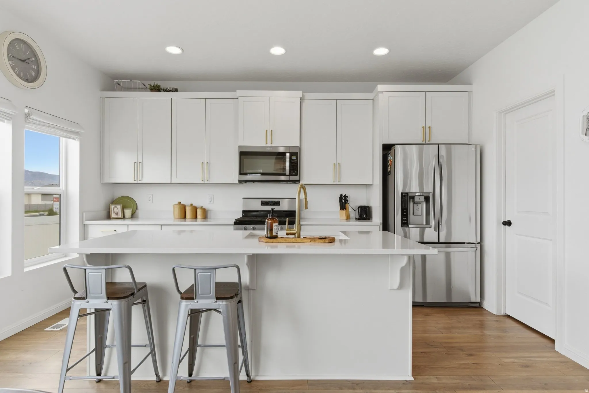 Modern kitchen featuring a central island with countertop seating, white cabinetry with gold-tone hardware, stainless steel appliances, recessed lighting, and wood-finish flooring