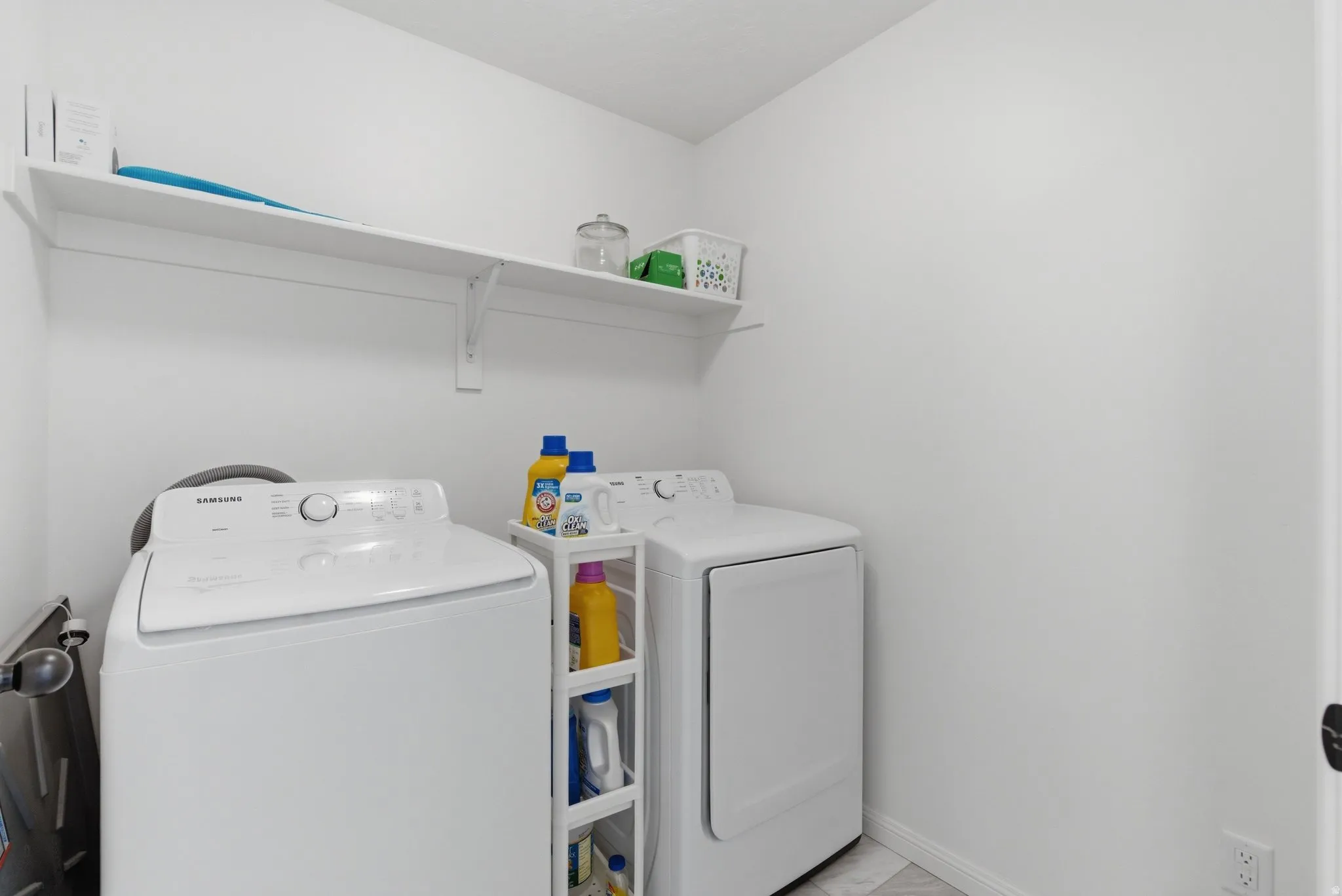 Laundry area featuring a top-load washing machine, front-load dryer, wall-mounted shelving, and light-toned flooring