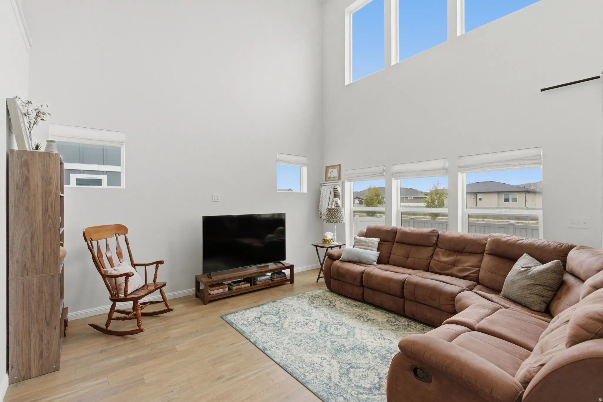 Vaulted ceiling living space featuring high transom windows, wood-finish flooring, and multiple lower windows providing natural light