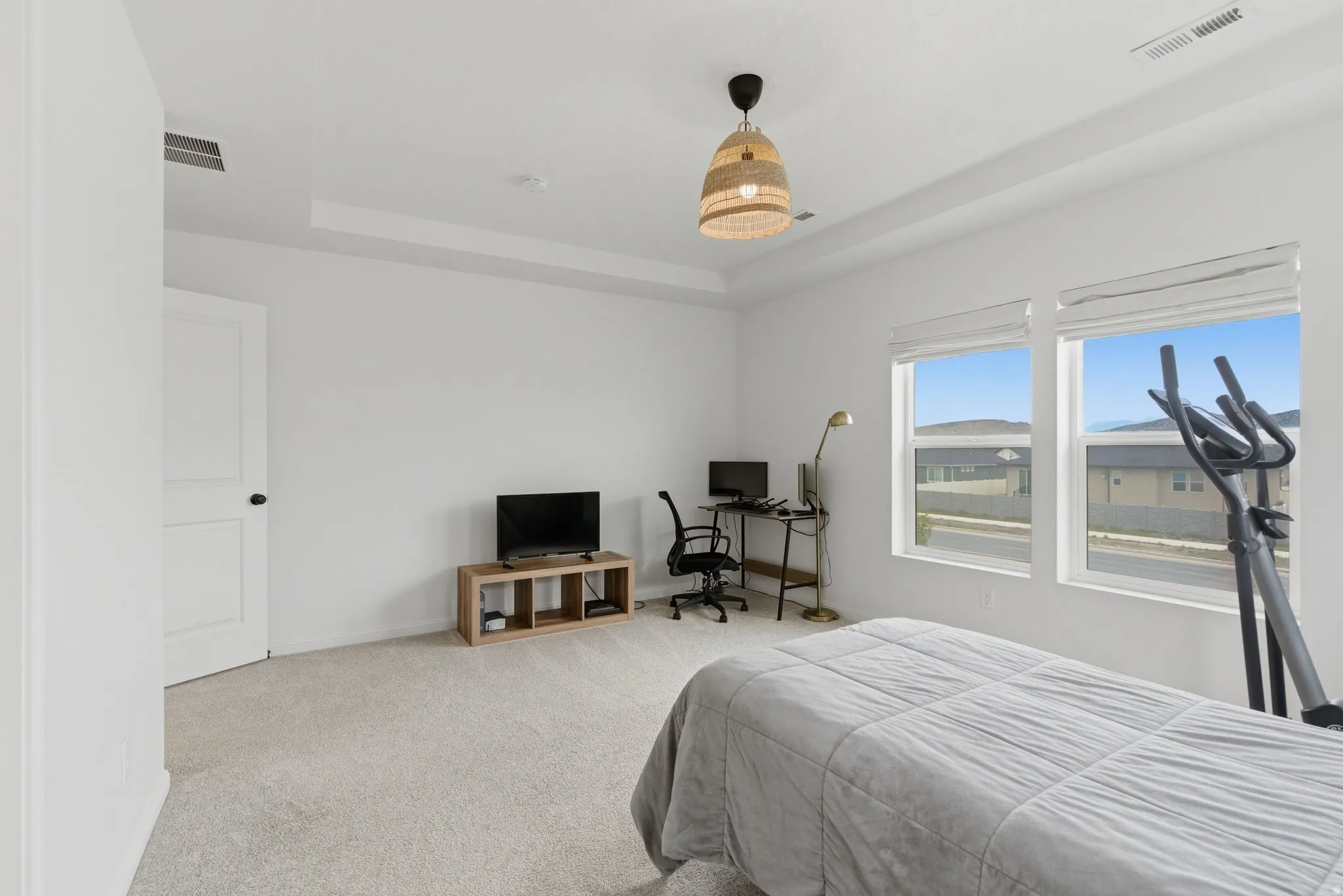 Room featuring a tray ceiling, light-colored carpeting, and two large windows with white blinds