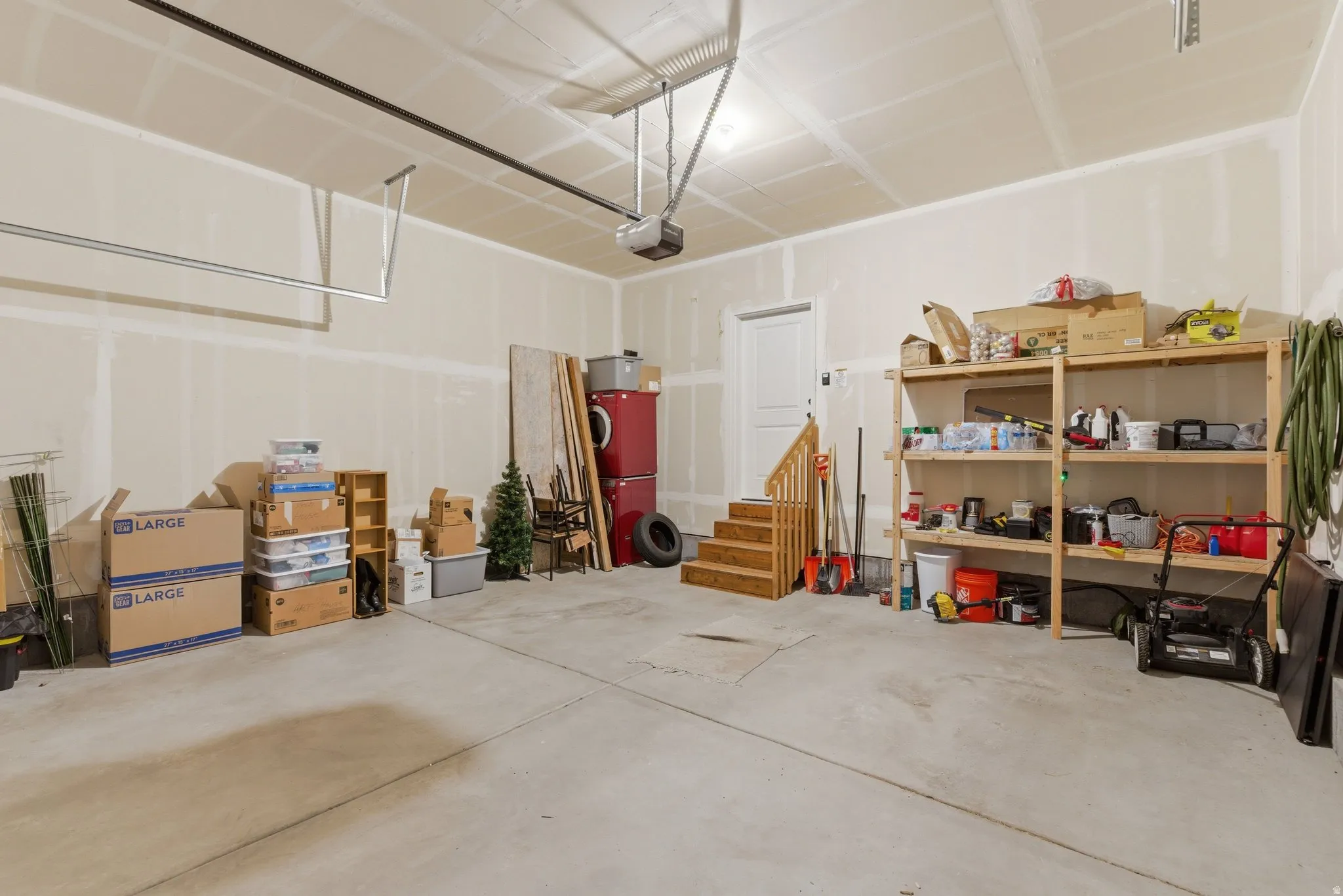 Spacious garage featuring a concrete floor, exposed ceiling joists, and a white interior door with wooden stairs