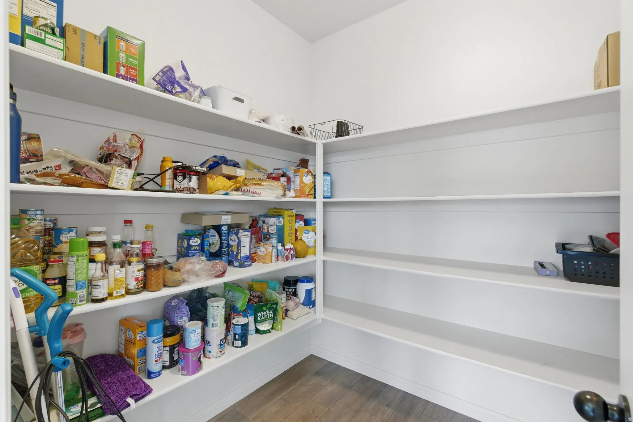 Corner pantry featuring multiple white built-in shelves, wood-finish flooring, and white walls