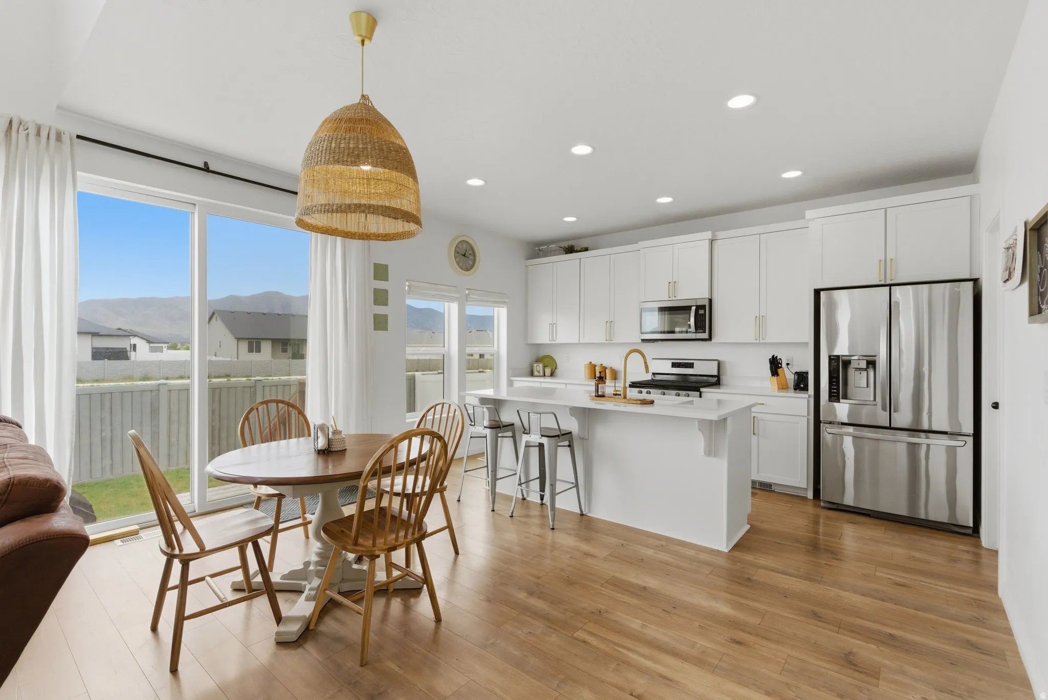 Open-concept kitchen and dining area featuring wood-finish flooring, white cabinetry, and stainless steel appliances