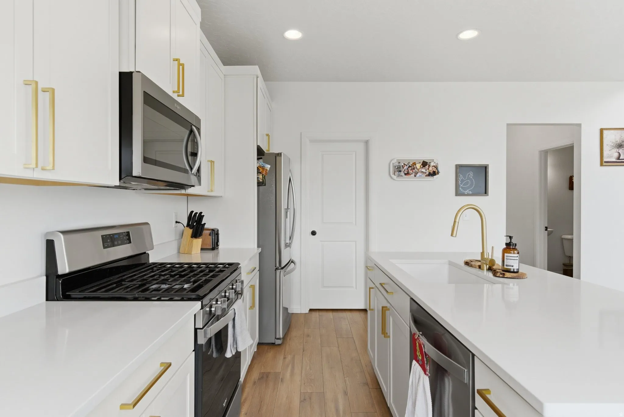 Modern kitchen featuring white cabinetry with gold-tone hardware, stainless steel appliances, light-toned countertops, a gas range, and wood-finish flooring