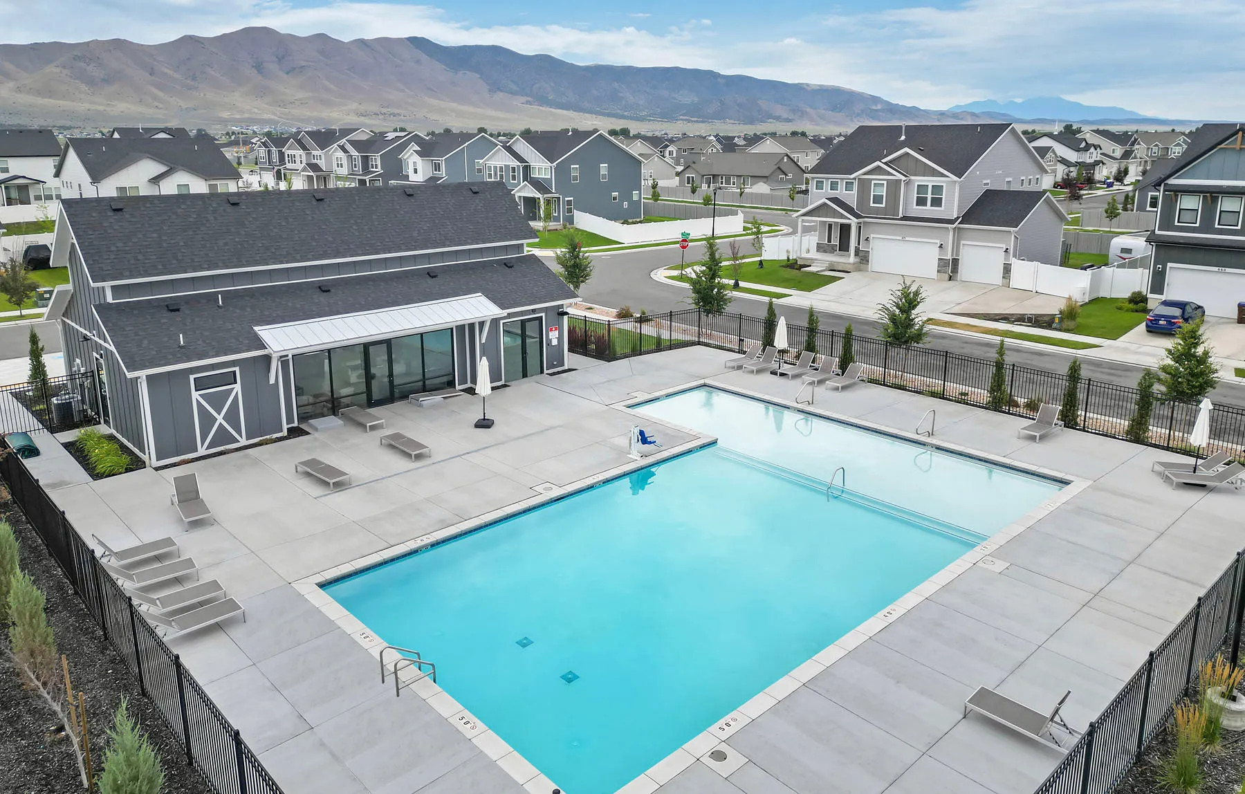 Community pool and amenity building featuring a contemporary gray exterior with white trim, large windows, and an expansive concrete sundeck