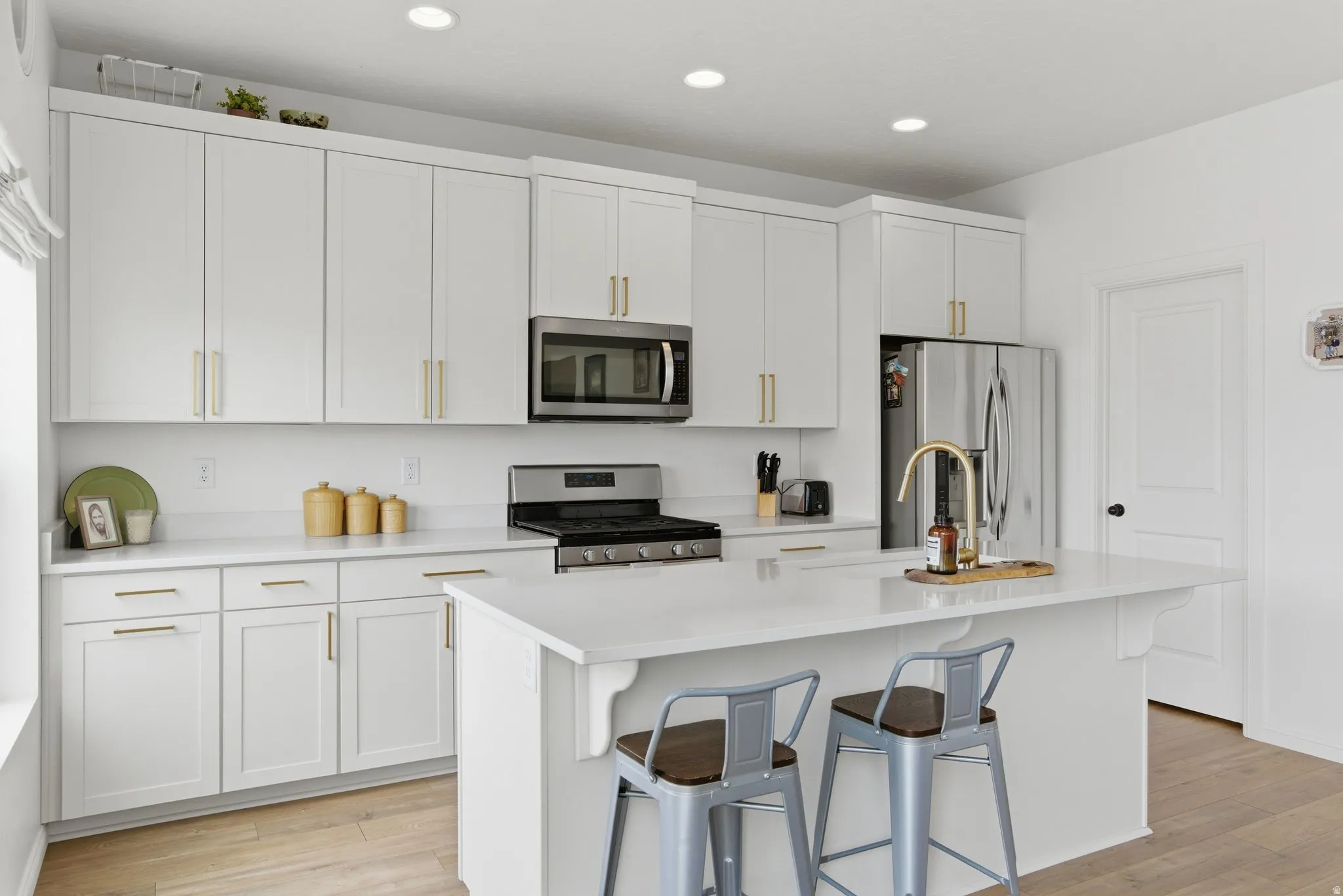 Modern kitchen featuring white cabinetry, stainless steel appliances, a center island with countertop seating, recessed lighting, and wood-finish flooring