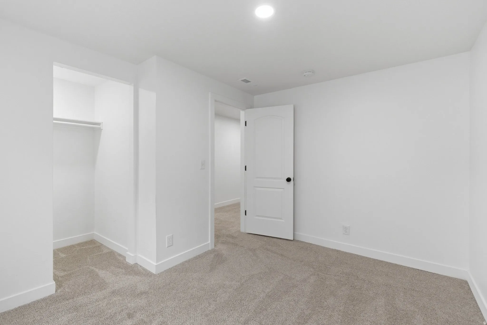Spacious room featuring neutral carpeting, a built-in closet with shelving, a white paneled door with black hardware, recessed lighting, and white baseboards