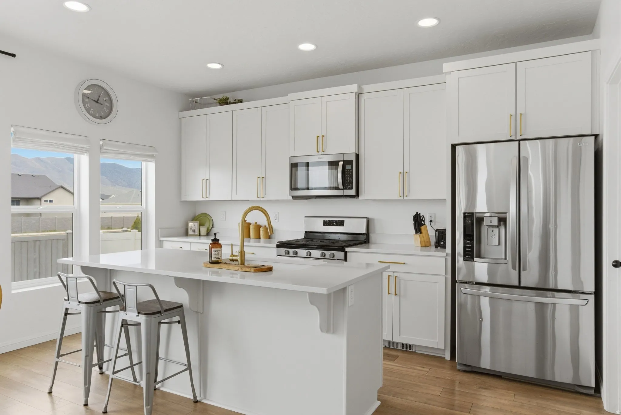 Modern kitchen featuring white shaker cabinetry with gold-finish hardware, stainless steel appliances, and a central island with a sink and seating